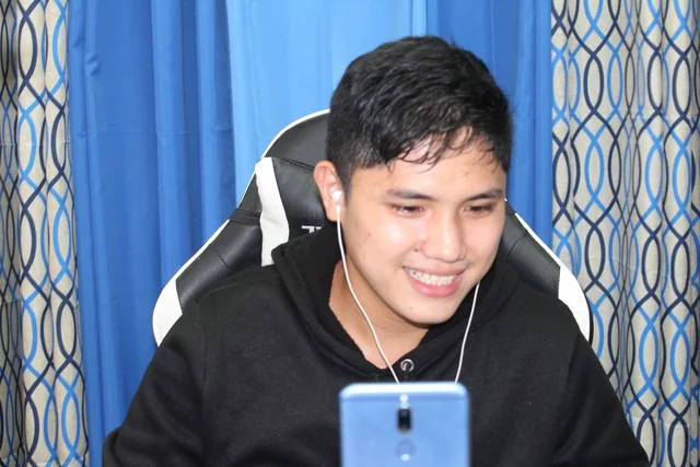 Rechcel smiling in a black hoodie with earbuds and a phone in front of him