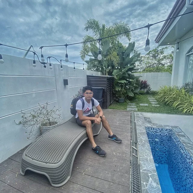 Rechcel with a backpack seated on a lounge chair beside a pool